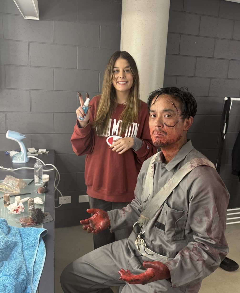 Behind the scenes — bloodied actor in coveralls with Lara on set