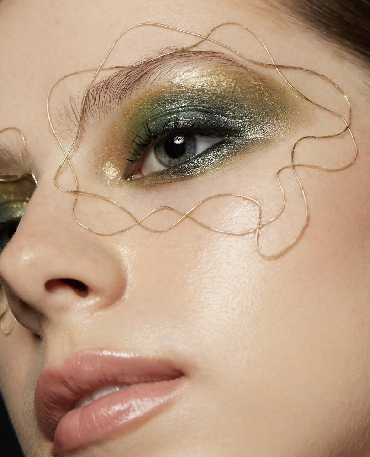 Editorial close-up — green and gold eye with gold wire art