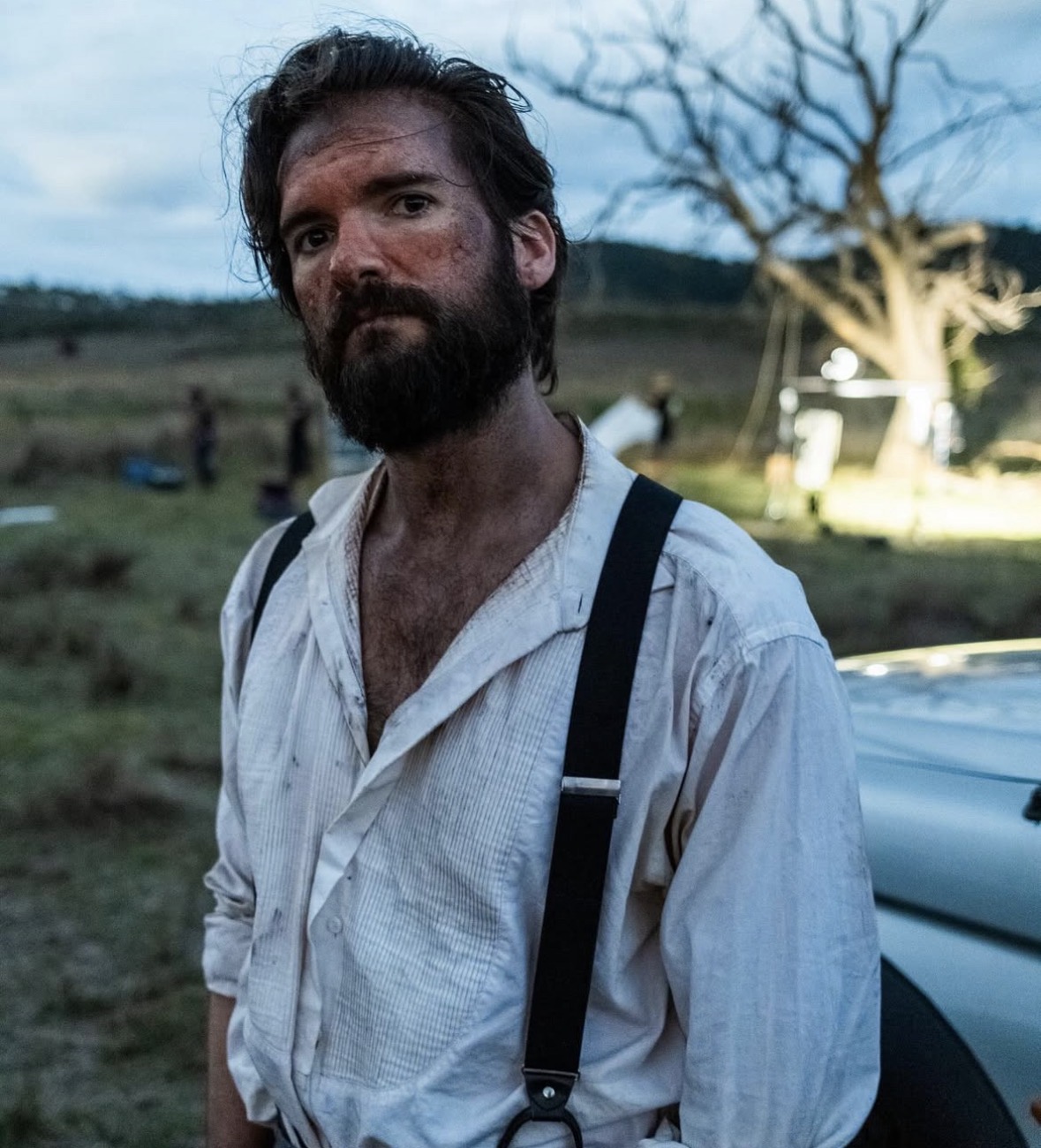 Film still — weathered character at dusk with grime and stubble