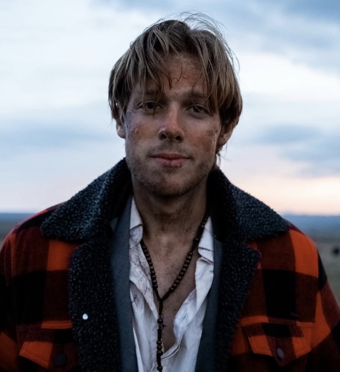 Film still — windswept character with dirt and abrasions at dusk